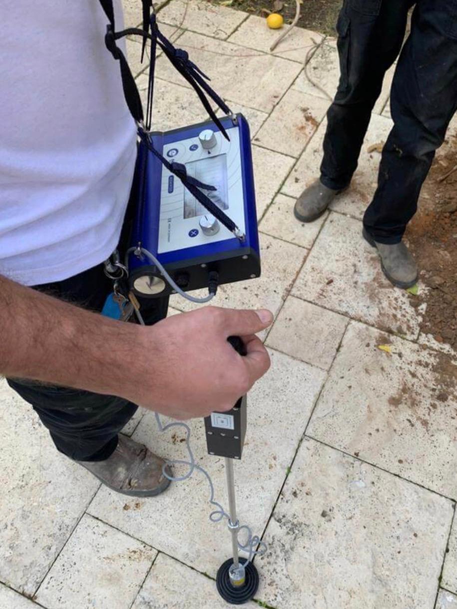טכנאי SOS מאתר נזילה עם גלאי אקוסטי על ריצוף בחצר